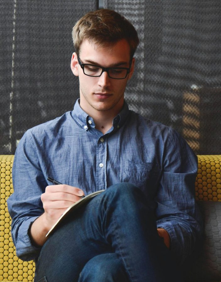entrepreneur-startup-start-up-man-39866-39866 A young man in glasses writes in a notebook while sitting on a stylish couch indoors.