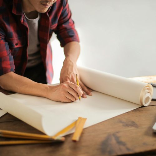 pexels-photo-3760529-3760529 A focused architectural designer drafting blueprints at a desk indoors.
