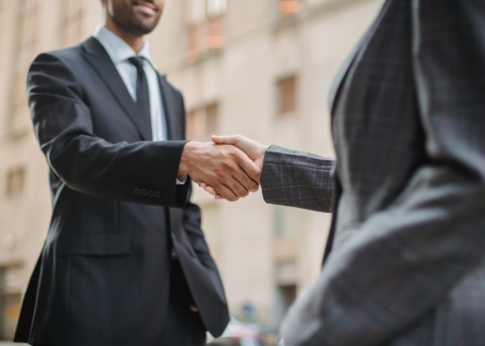 Business professionals greeting each other with a handshake outdoors, symbolizing partnership.